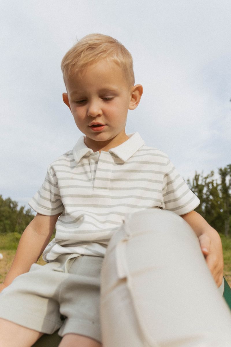 Young boy in a striped shirt and shorts sitting outdoors with a blurred background