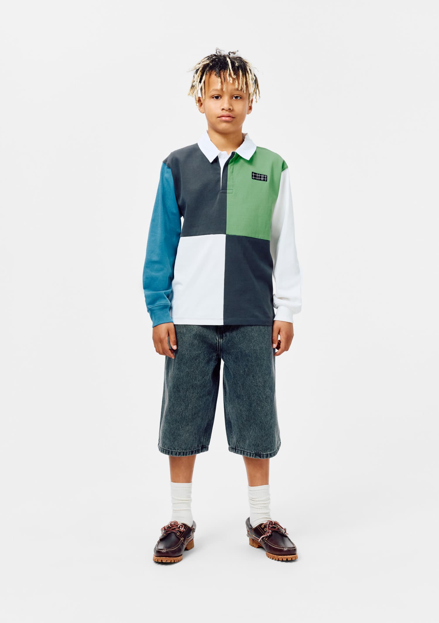 Child wearing a colorful patchwork shirt and denim shorts on a white background