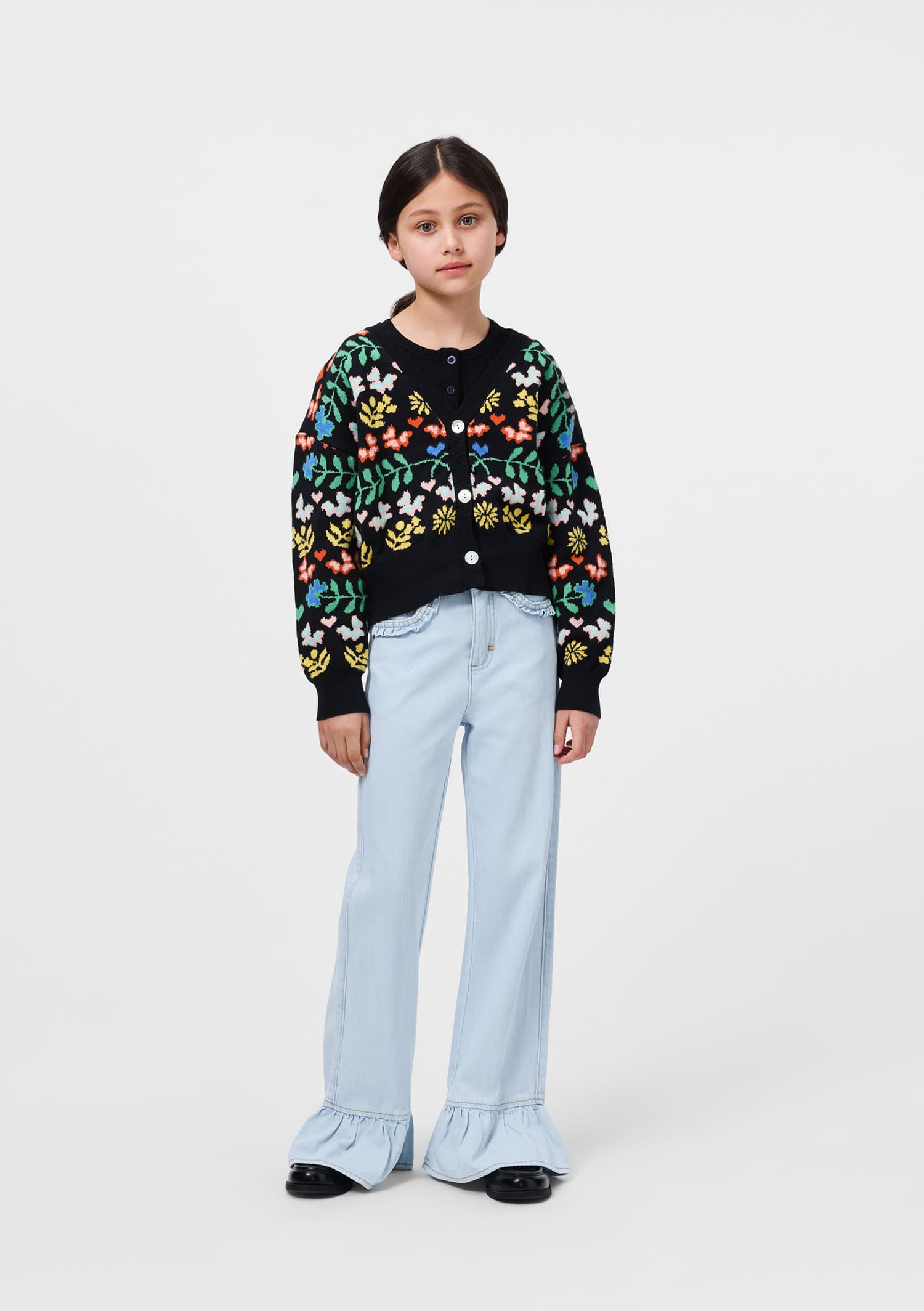 Child wearing a colorful floral-patterned sweater and light blue jeans on a white background