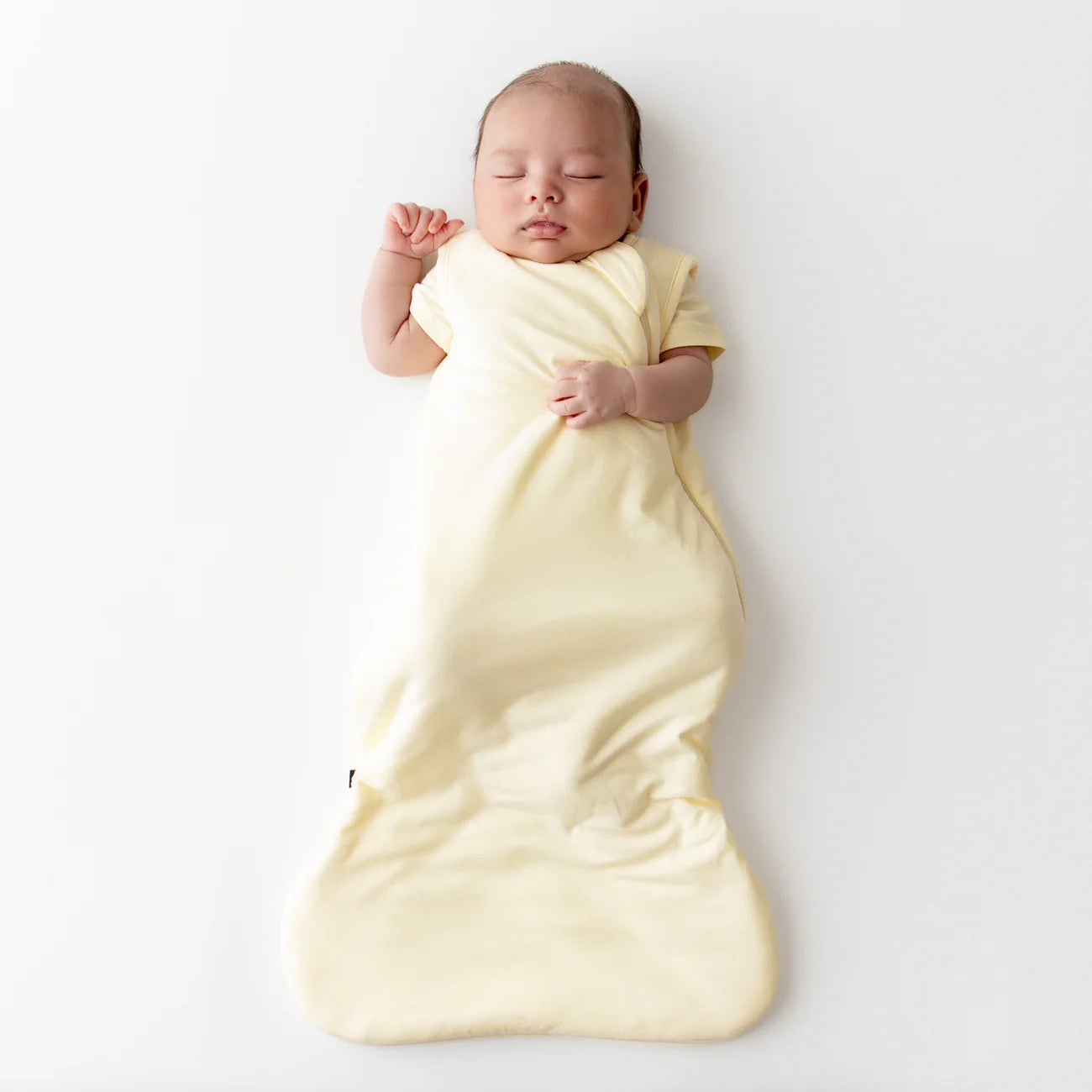 Newborn baby wrapped in a yellow sleep sack on a white background