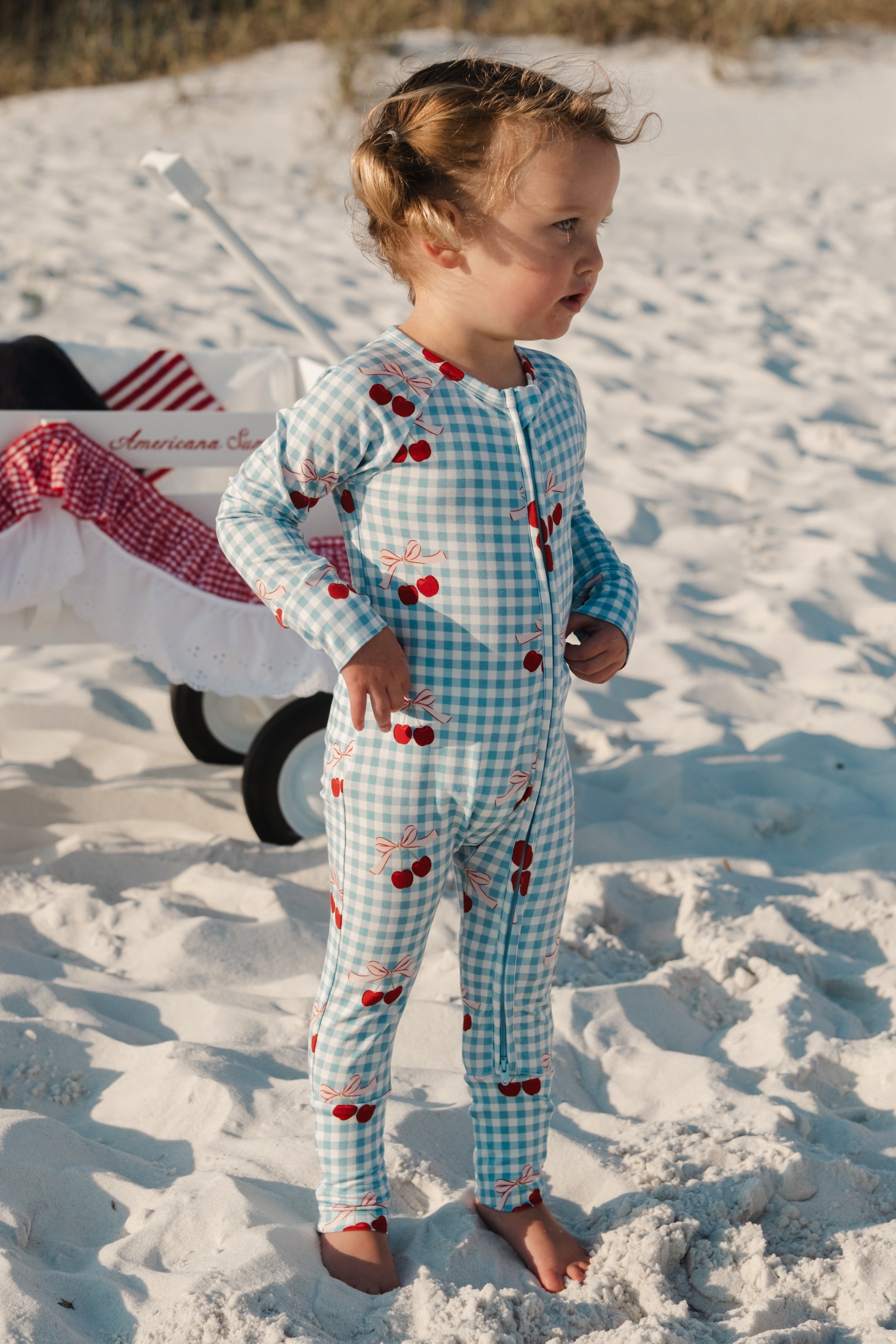 Child in a blue gingham onesie with a cherry and bow pattern