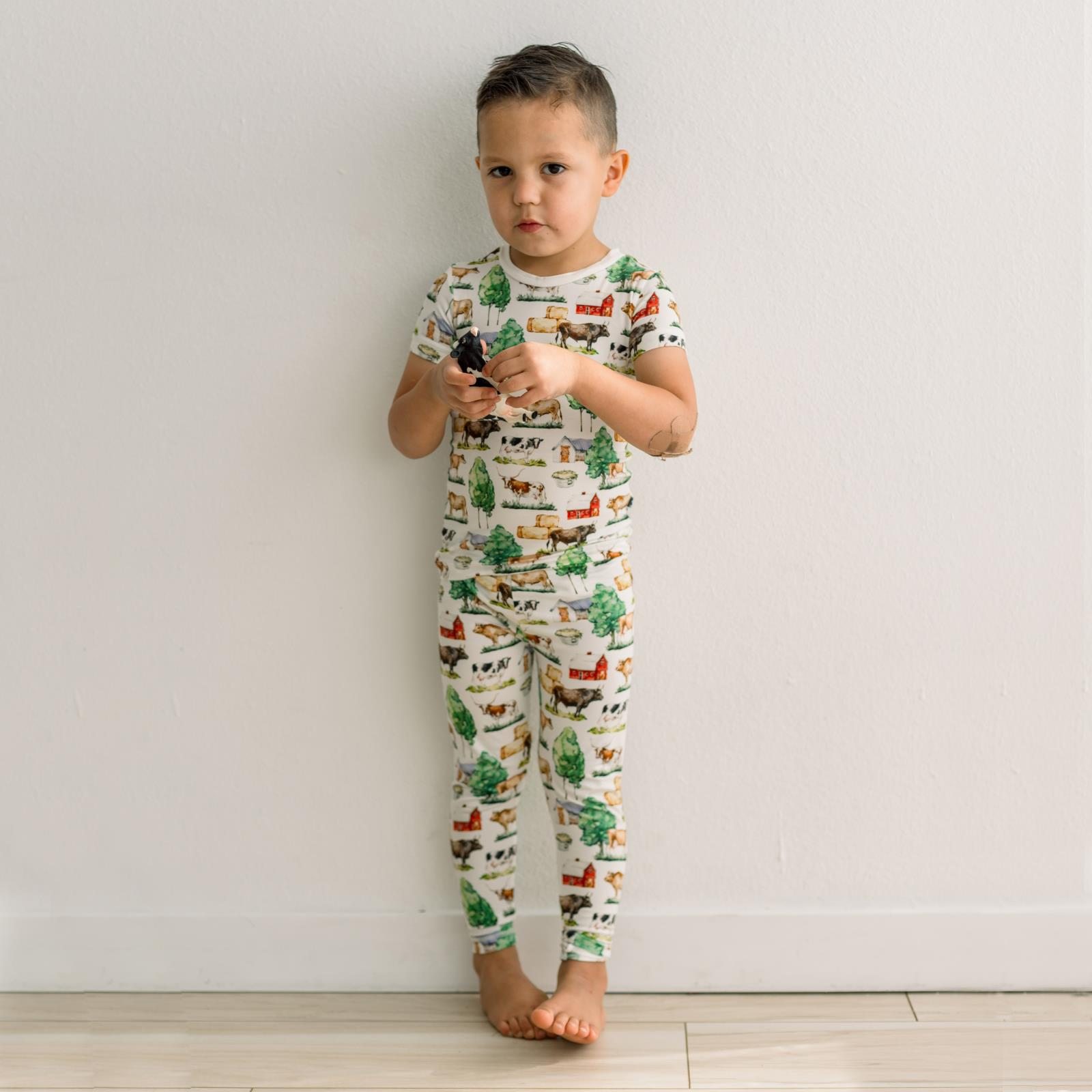 Child wearing a pajama set with a farm animal print against a plain background