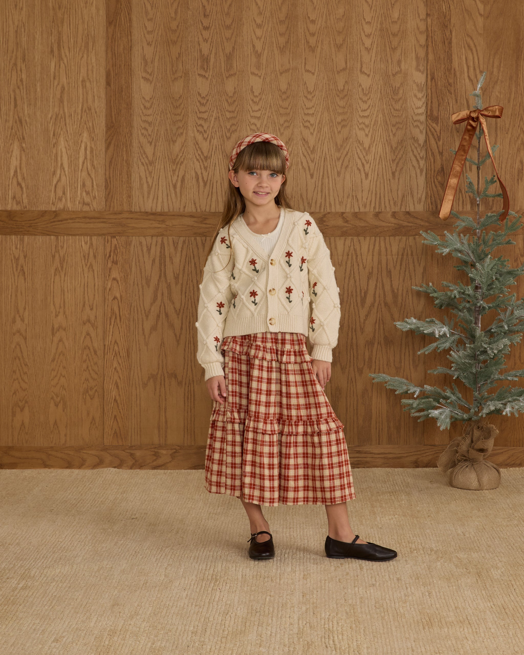 Young girl in a boxy crop cardigan with a red floral pattern and buttons.