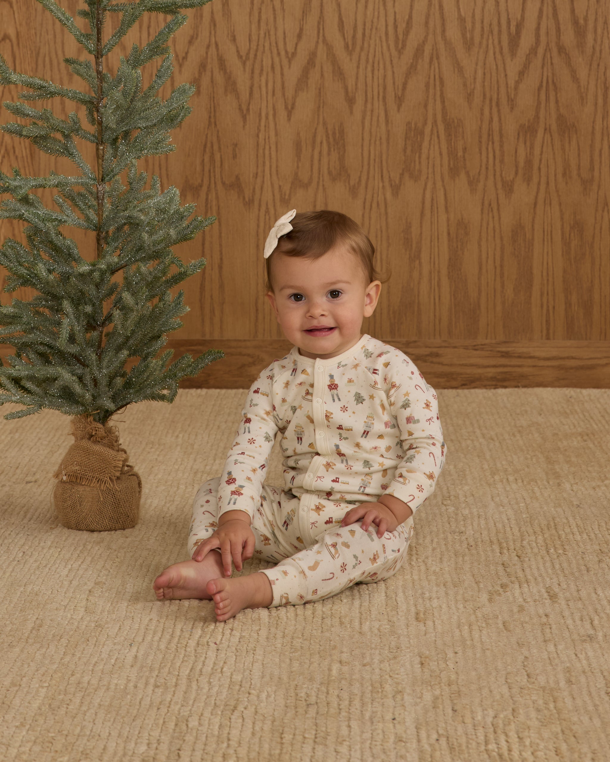 Baby wearing a white holiday romper sitting on a beige rug