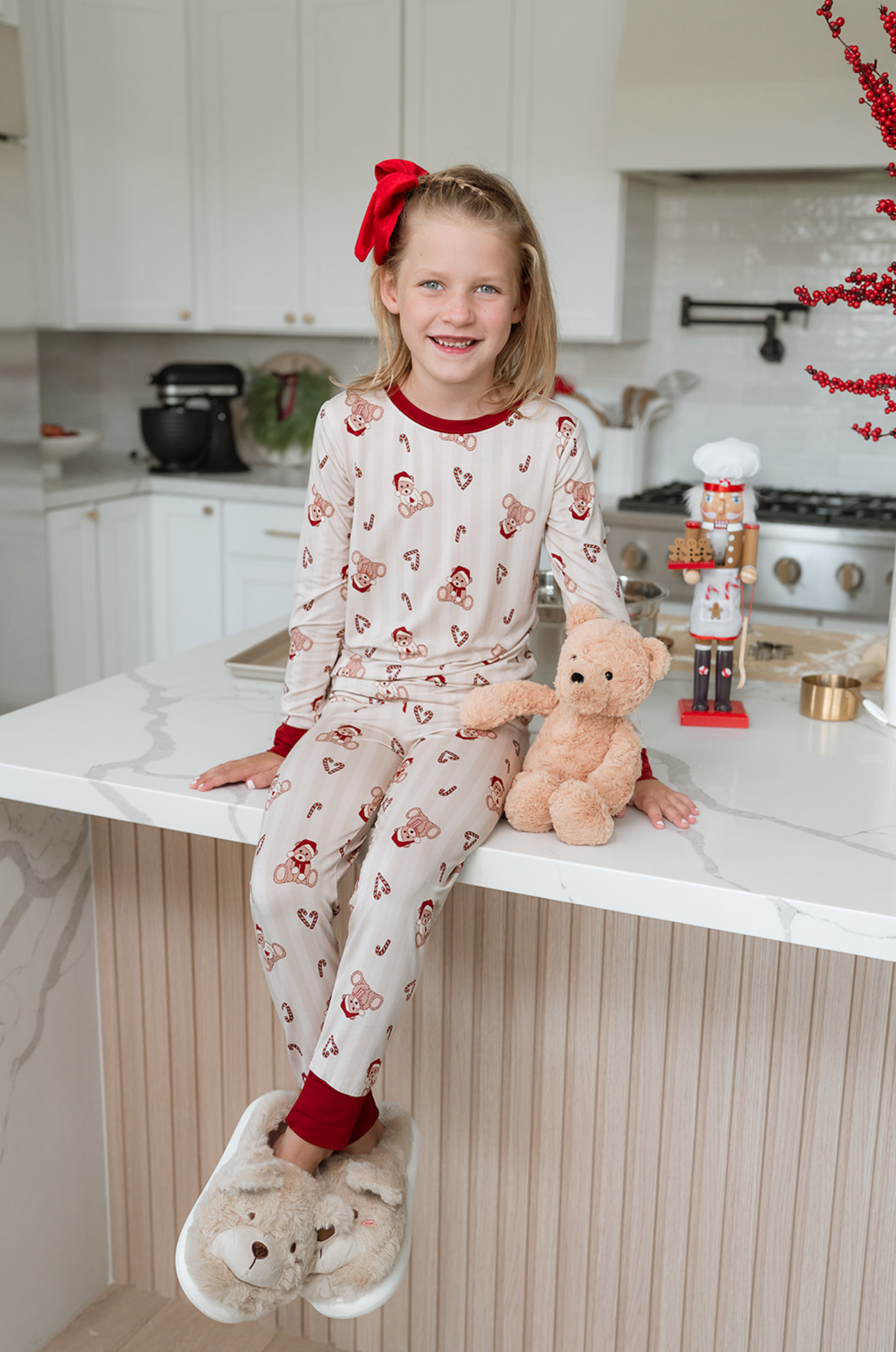 Young girl in pajamas sitting on a kitchen counter with a teddy bear