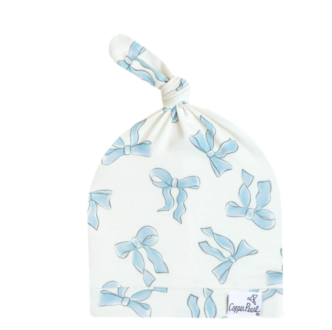A white top knot hat with blue bows and a branded label on the brim.