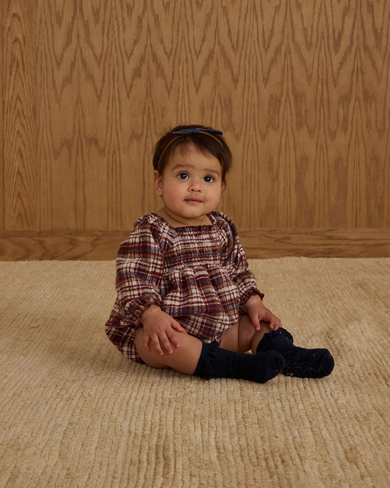 baby sitting on floor in burgundy plaid romper