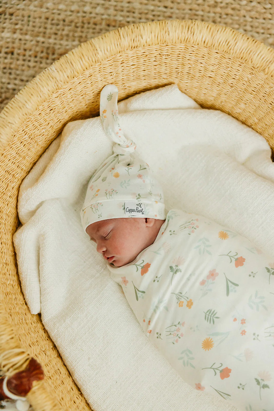 baby laying in basinet with floral swaddle and knotted hat