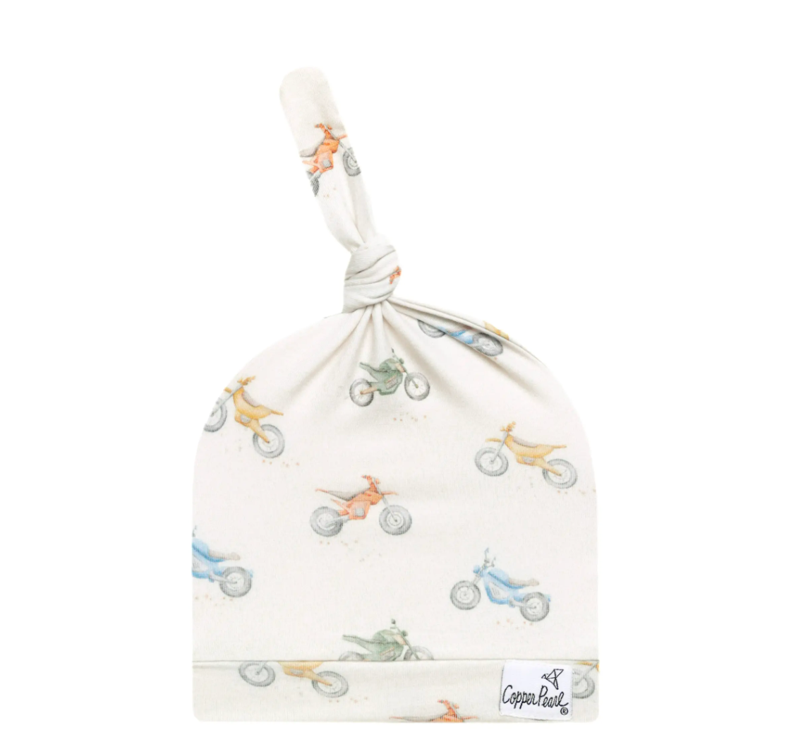 A beige baby top knot hat with a pattern of dirt bikes