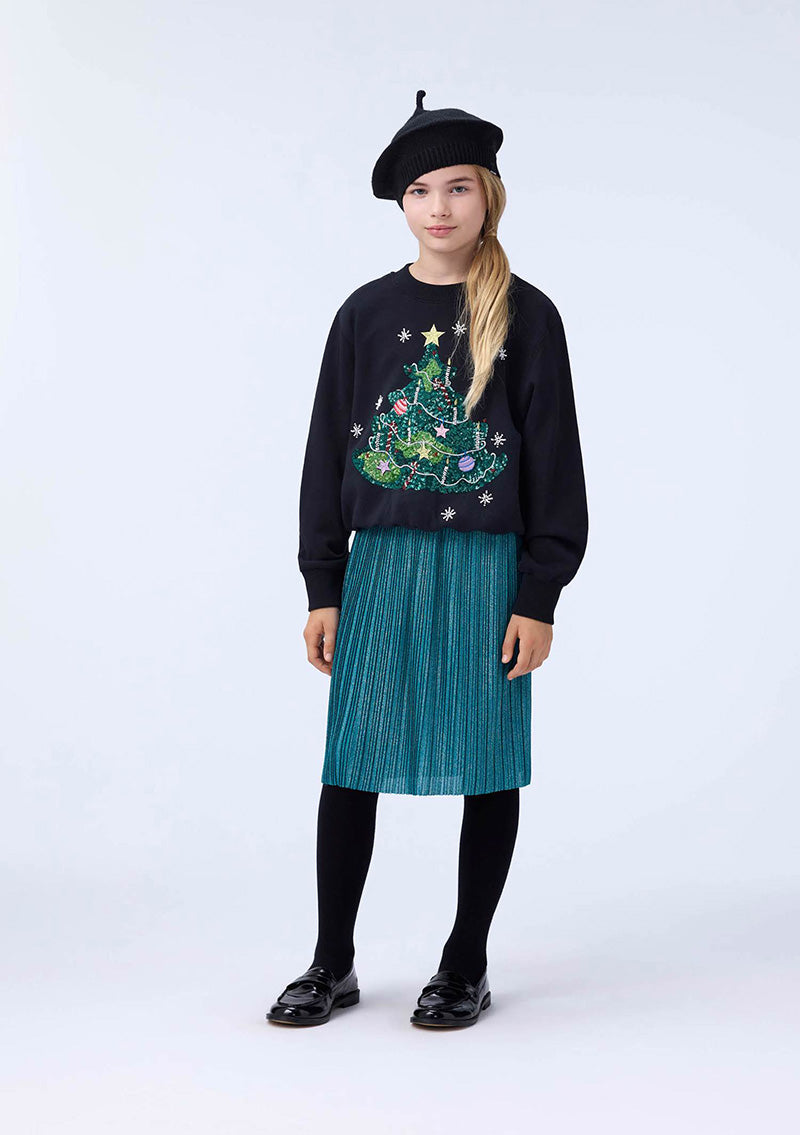 Person wearing a black sweater with a Christmas tree design, teal skirt, and black beret on a white background