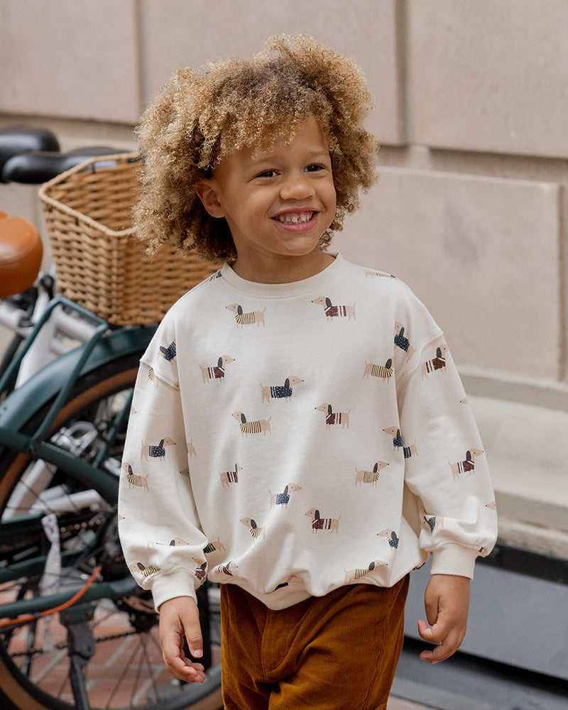 Child wearing a wiener dog patterned shirt standing next to a bicycle