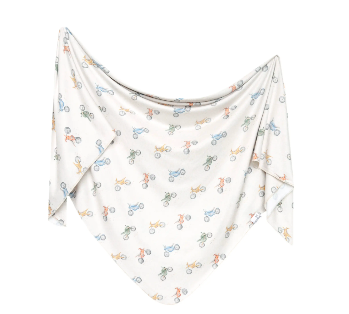 A knit swaddle blanket with a geometric pattern featuring bicycles in multiple colors on a white background.