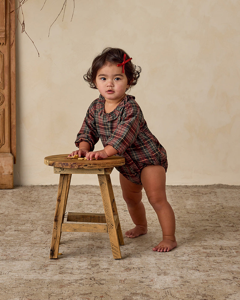 Child in a red plaid romper with a ruffled collar