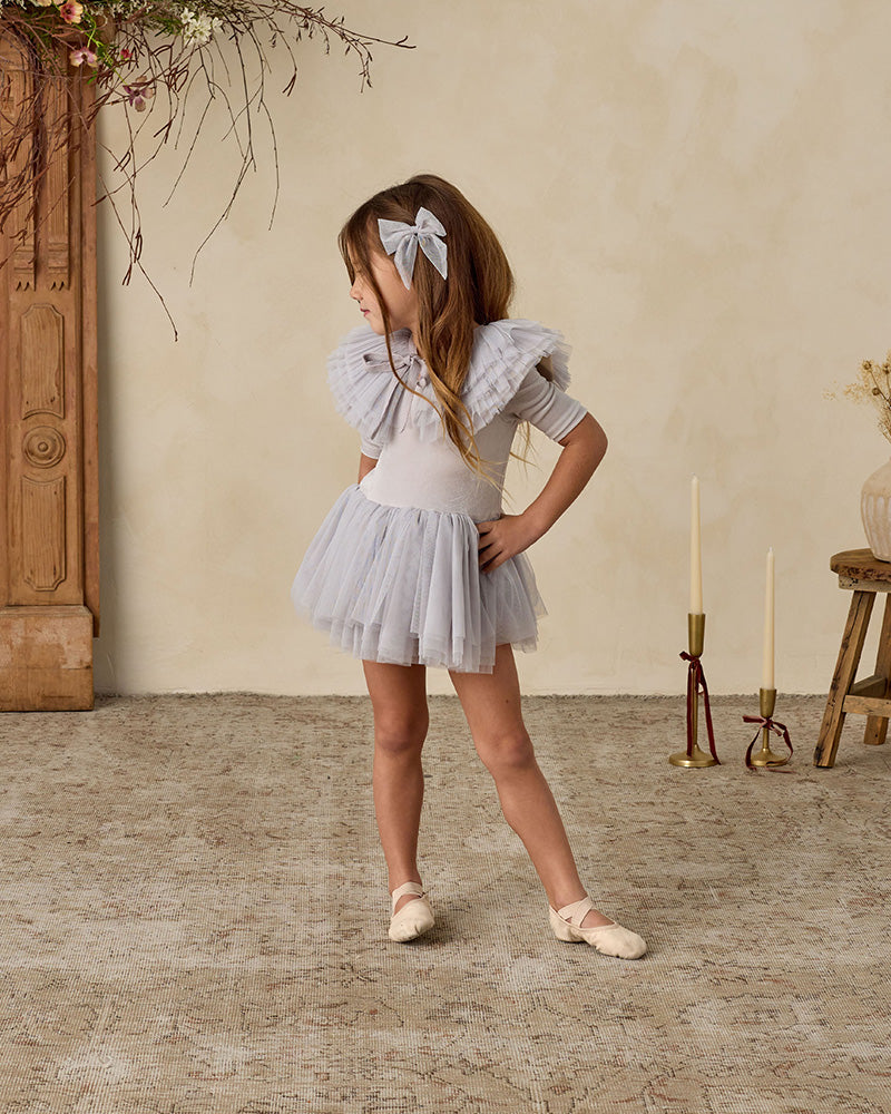 Young girl in a gray dress with ruffled sleeves and a scooped neck.