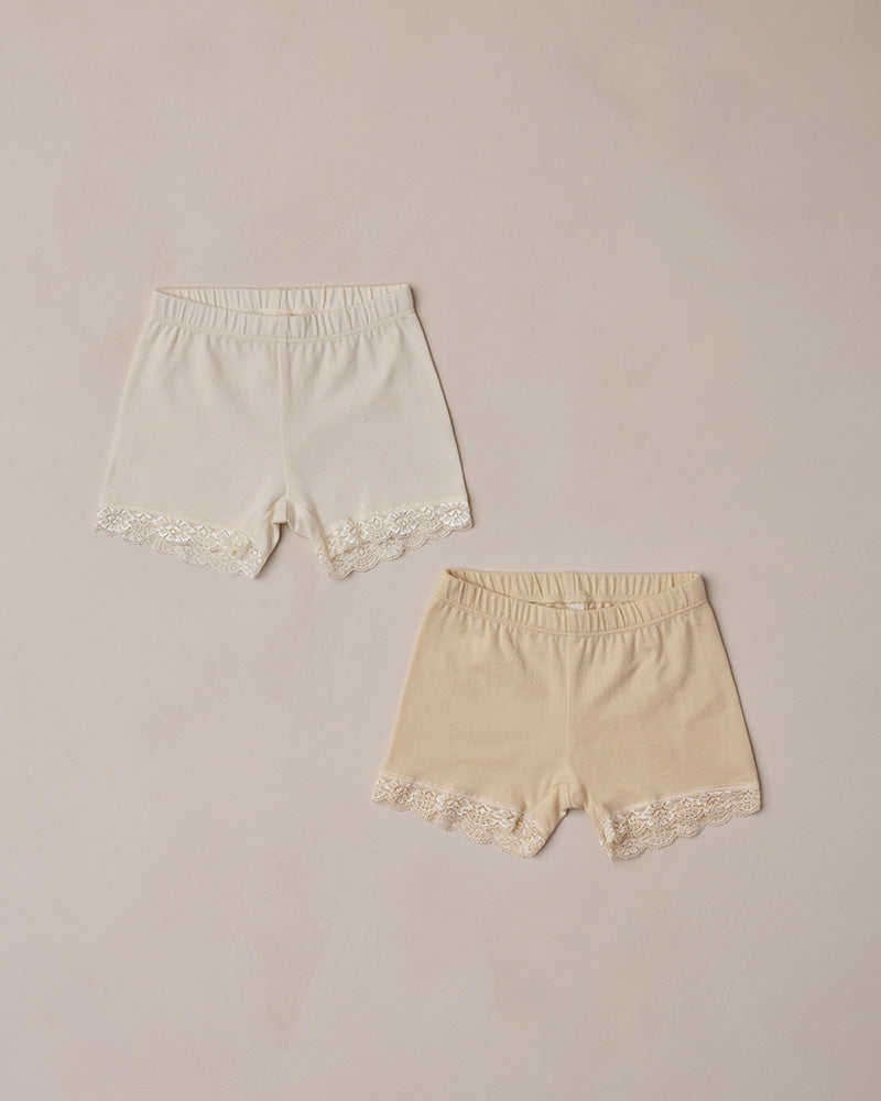 Two pairs of lace-trimmed shorts on a beige background