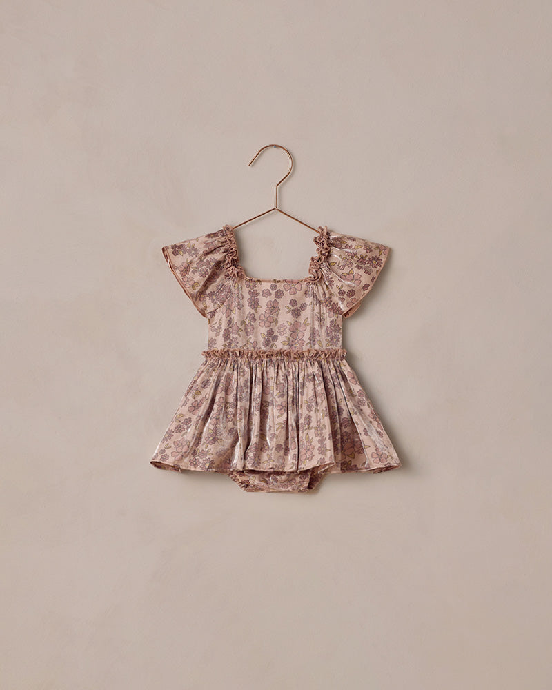 Floral baby romper on a hanger against a beige background