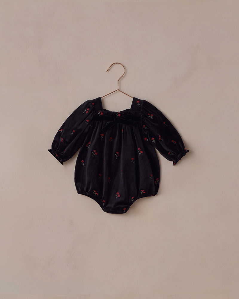 Black baby romper with a red floral pattern on a beige hanger against a beige background