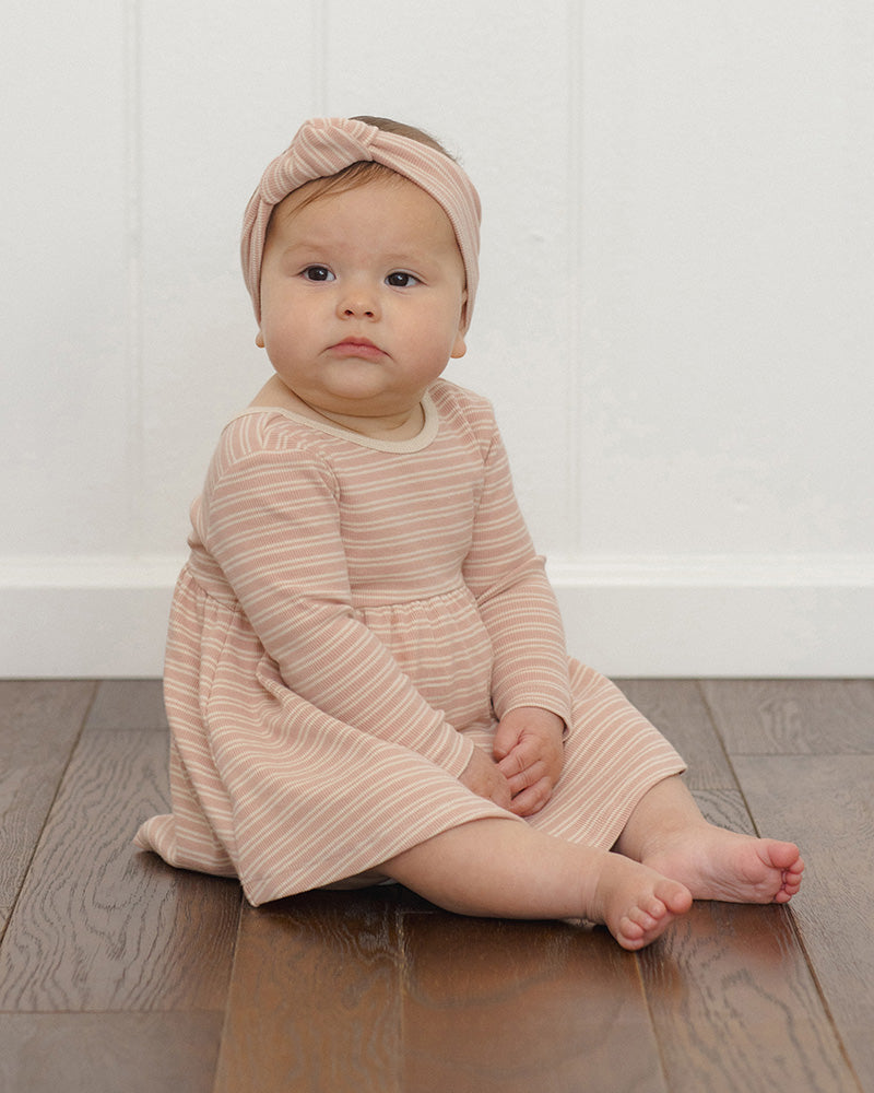 A long-sleeve baby dress with a pleated skirt, featuring horizontal stripes in dusty pink and cream, with a solid cream crew neck.