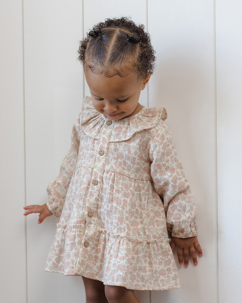 A toddler's long-sleeve button-up dress with a ruffled collar and a delicate pink and beige floral pattern, shown flat on a white background.