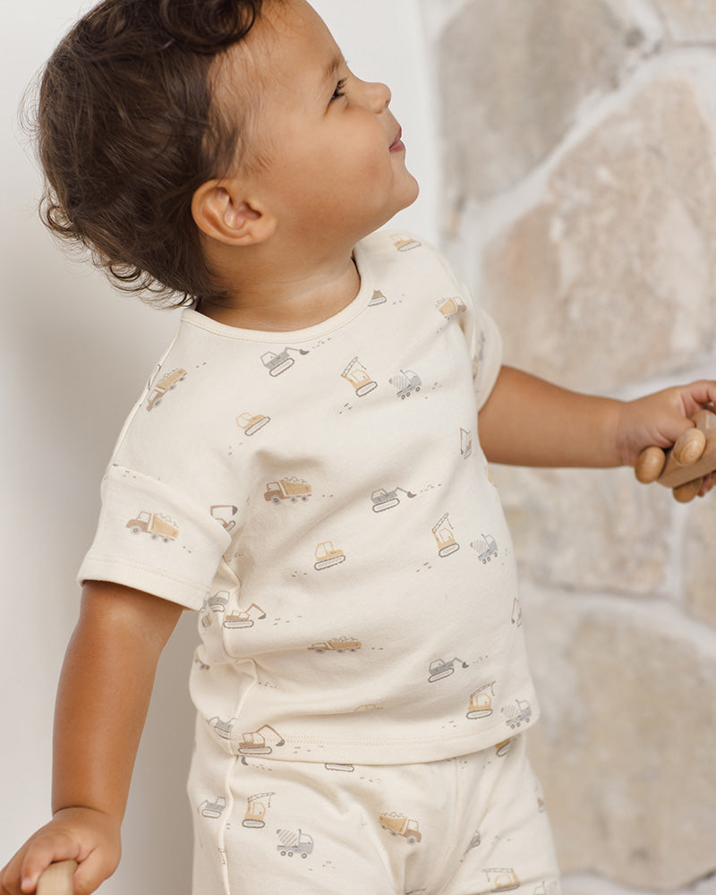 Child wearing a white shirt with small construction prints against a neutral background