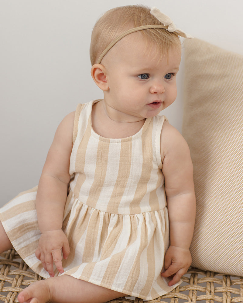 Baby wearing a striped dress sitting on a textured surface.