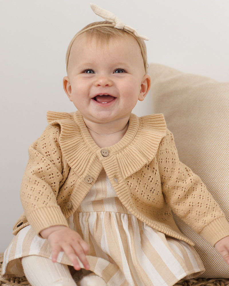 Baby wearing a beige knitted cardigan with a ruffled collar.