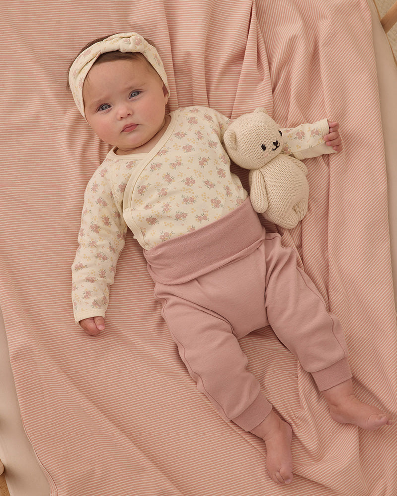Baby lying on a pink blanket wearing a floral onesie and pink pants.