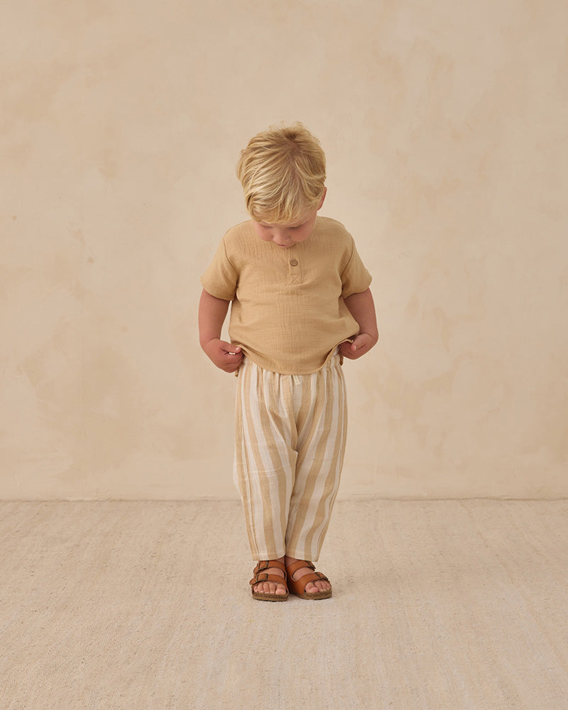 Young child wearing a beige shirt and striped pants on a plain background