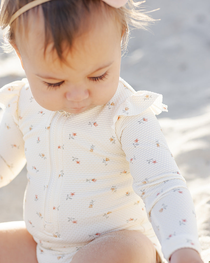 Baby in a floral rashguard sitting on sand