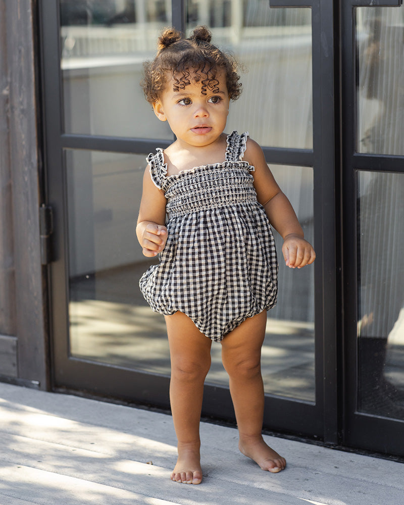 Child wearing a black and white gingham romper with a textured sleeve