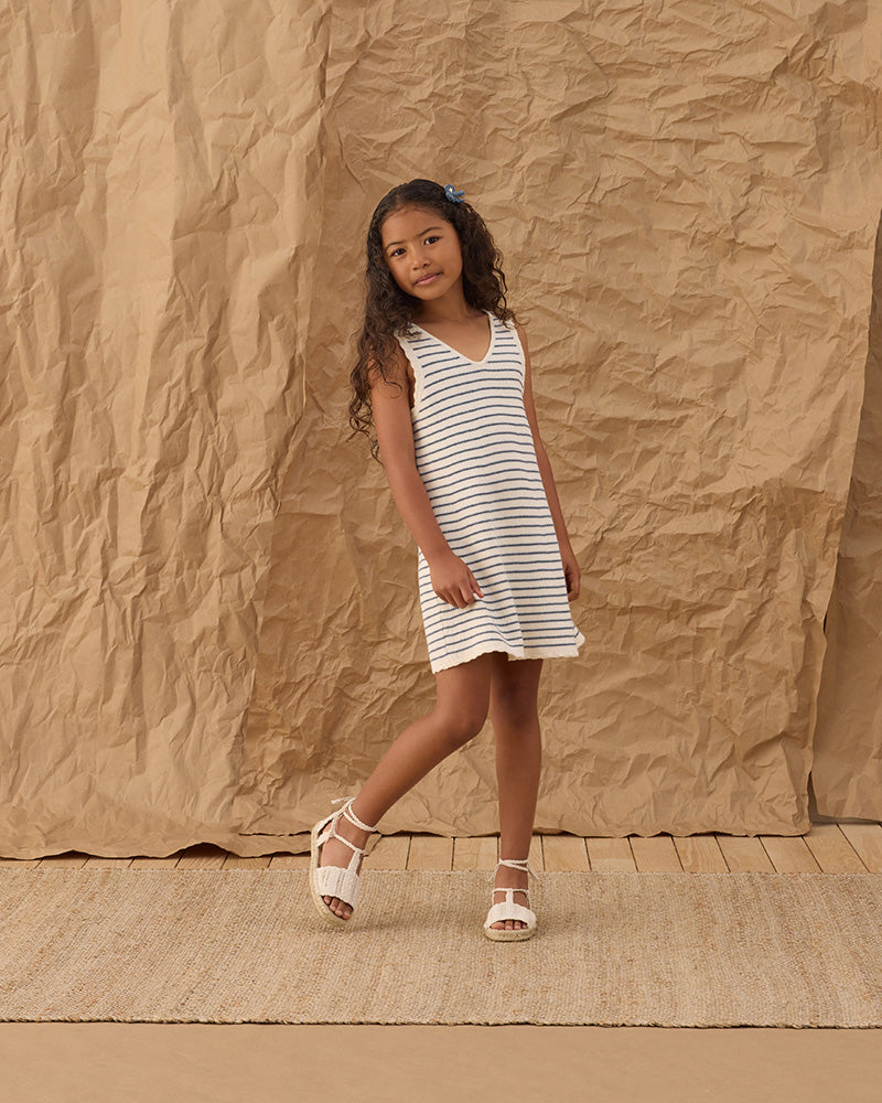 Young girl in a blue and white striped dress standing against a textured brown backdrop