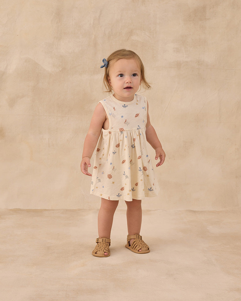 Young child wearing a nautical patterned dress on a beige background