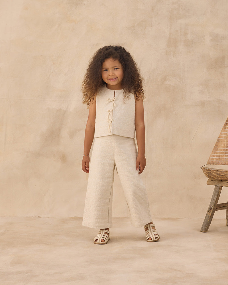 Young girl in a beige outfit standing against a beige background