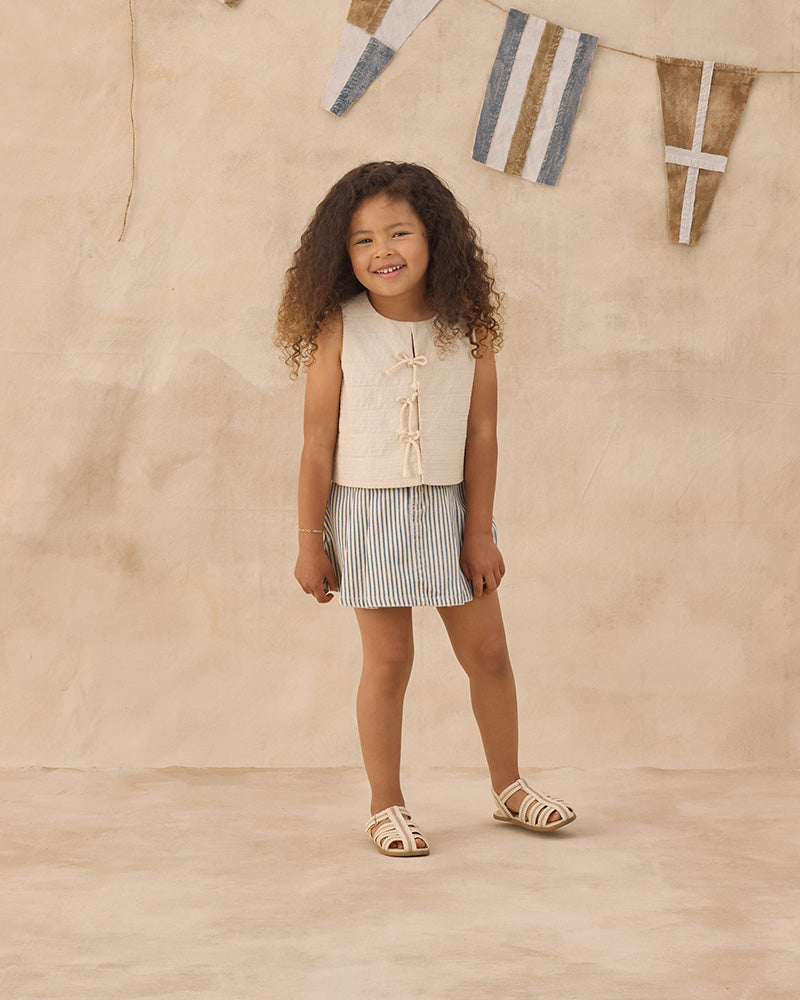 Young girl in a blue and white striped skirt against a beige background.