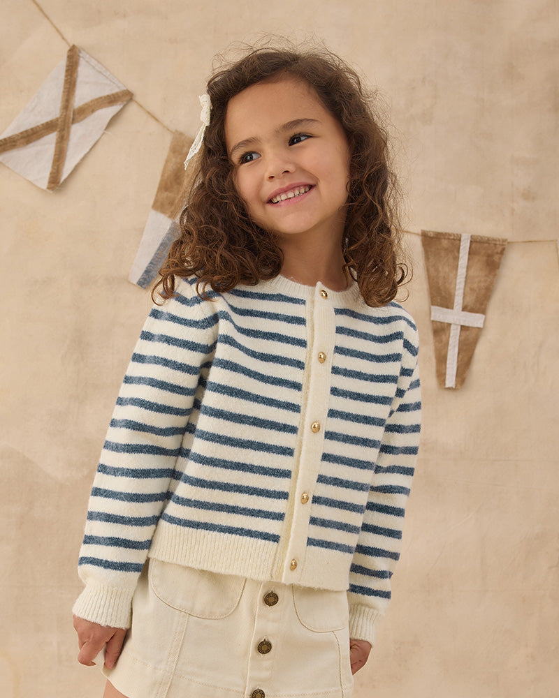 Child wearing a blue striped sweater with gold buttons against a beige background