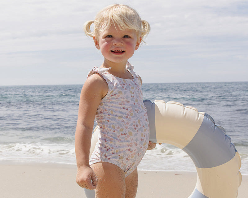 Child in a swimsuit standing on a beach with a life buoy.