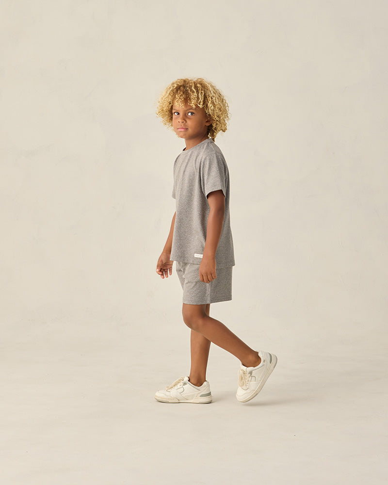 Child wearing a gray outfit with white sneakers on a beige background
