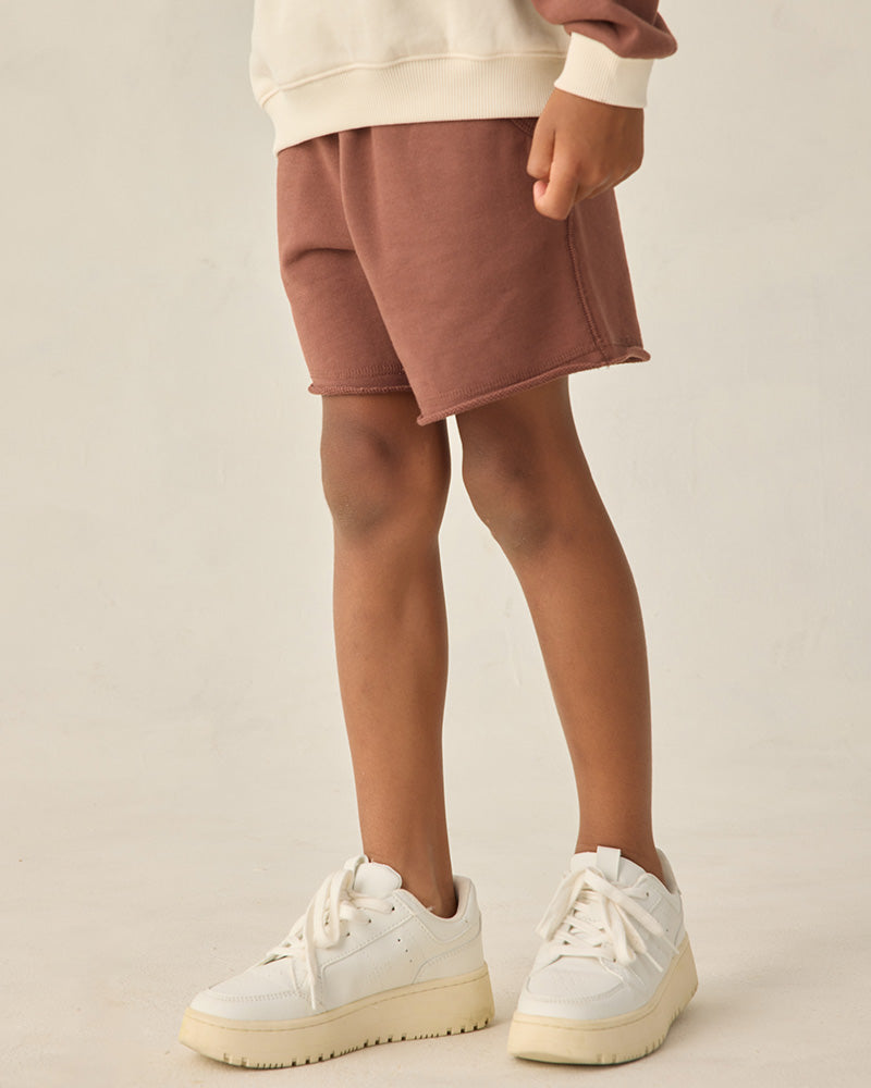 Child wearing brown jogger shorts against a white background.