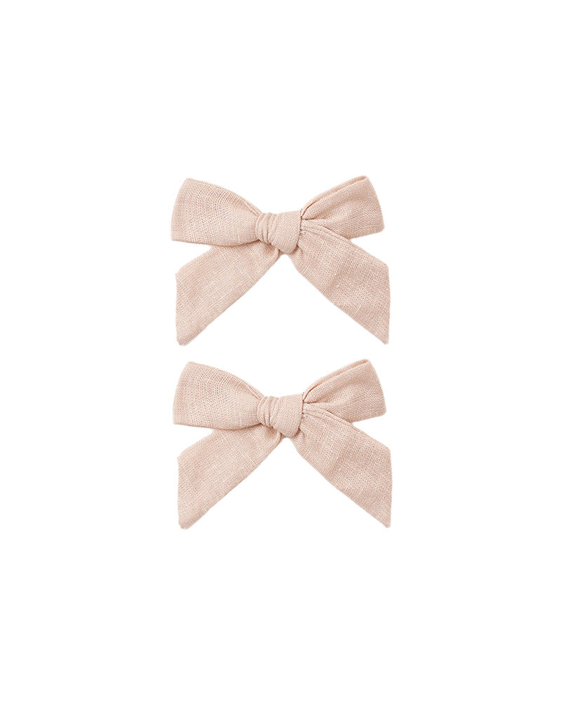 Two small bow hair clips in a light blush pink linen-like fabric.