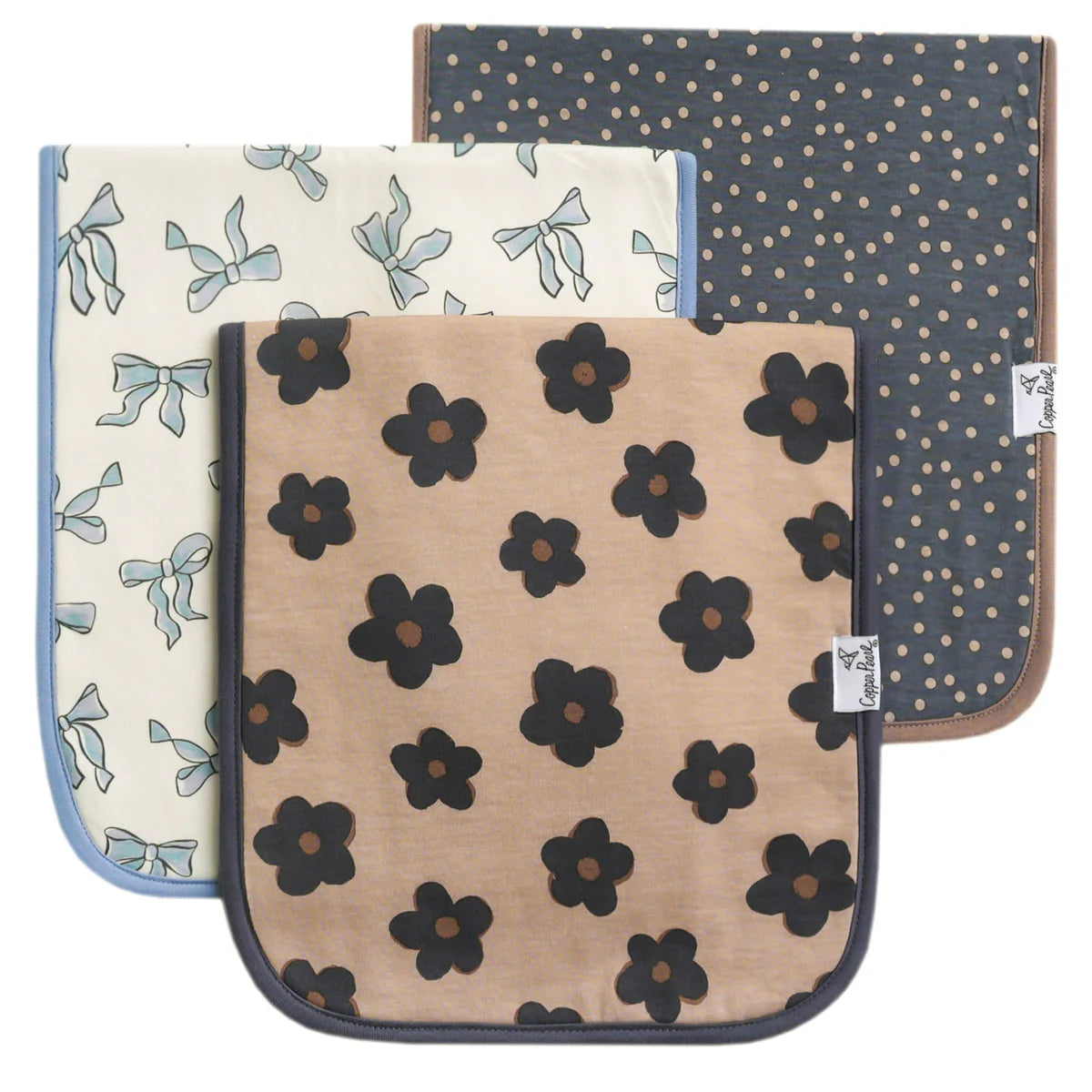 A set of three square burp cloths with different floral patterns. One has a blue background with white flowers, another is beige with black flowers, and the third is blue with a polka dot pattern.