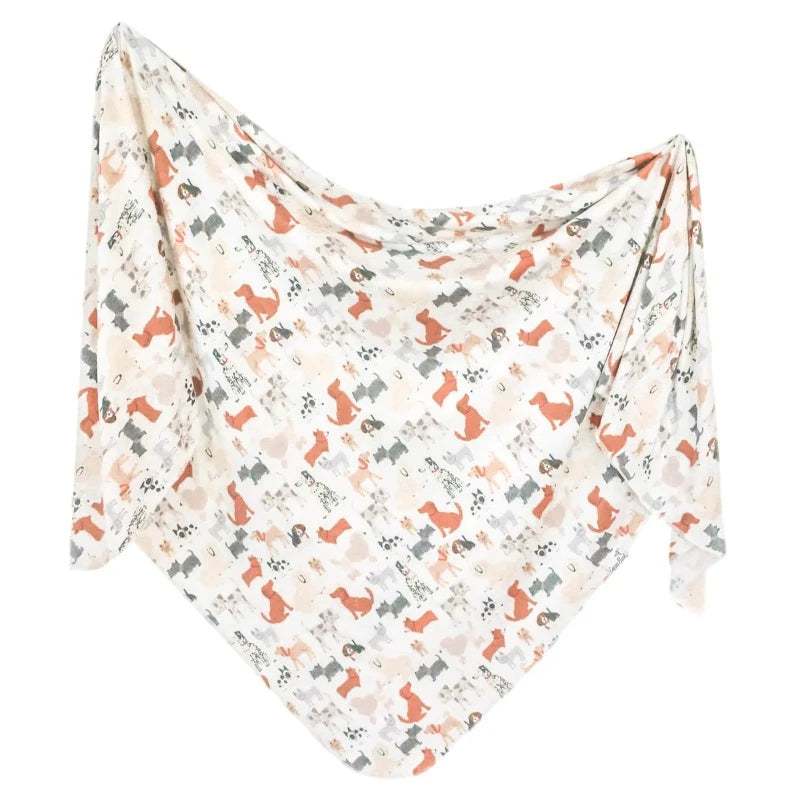 A knit swaddle blanket with a pattern of dogs, predominantly in a beige color with accents in gray and orange.
