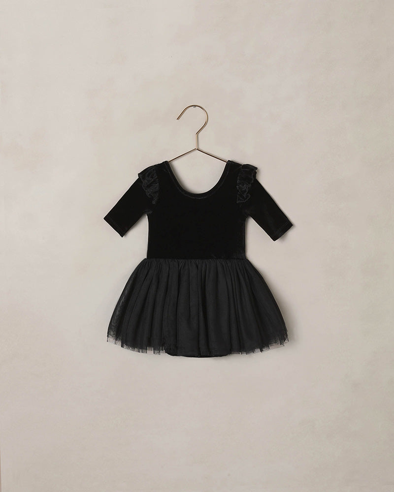 Black velvet dress with tulle skirt and a ruffle shoulder detail on a beige background