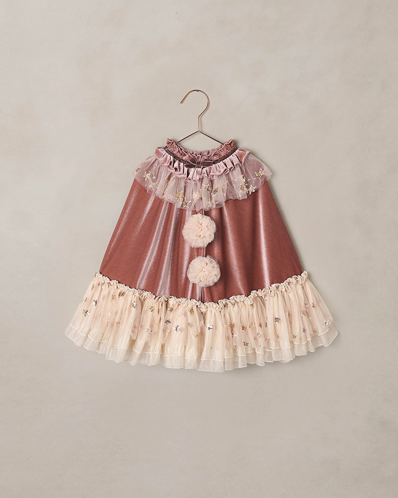 Children's costume cape with ruffles and star details on a beige background