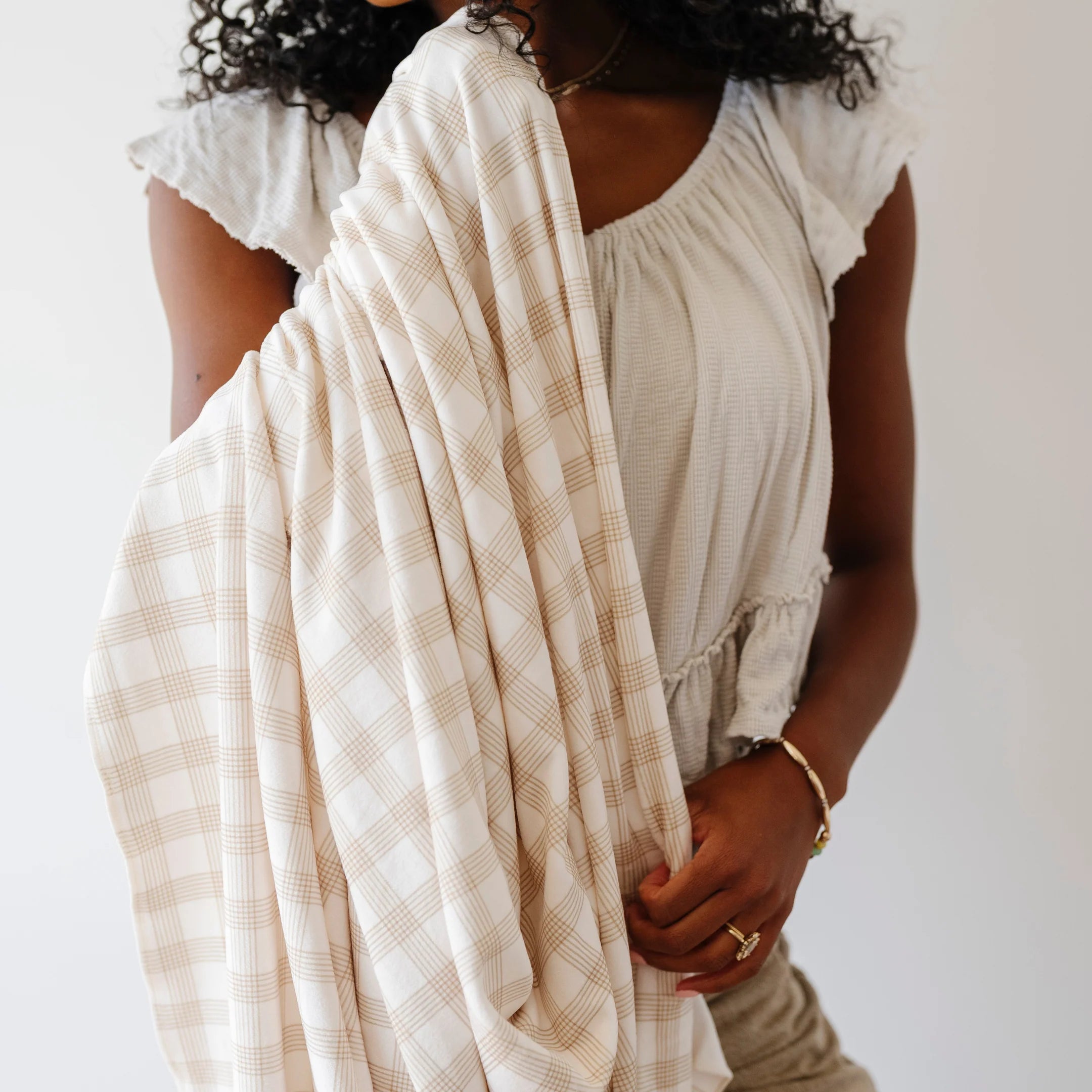 Woman holding a beige checkered blanket against a white background