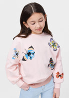 Young girl wearing a pink sweater with colorful butterfly designs on a white background