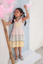 Young girl in a colorful layered dress holding cotton candy against a light blue door.