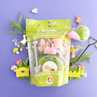 A Garden Kiddough Play Kit with green play dough and various small toy garden items including a garden goose, mushroom, snail charm, and a watering can, displayed on a purple background.