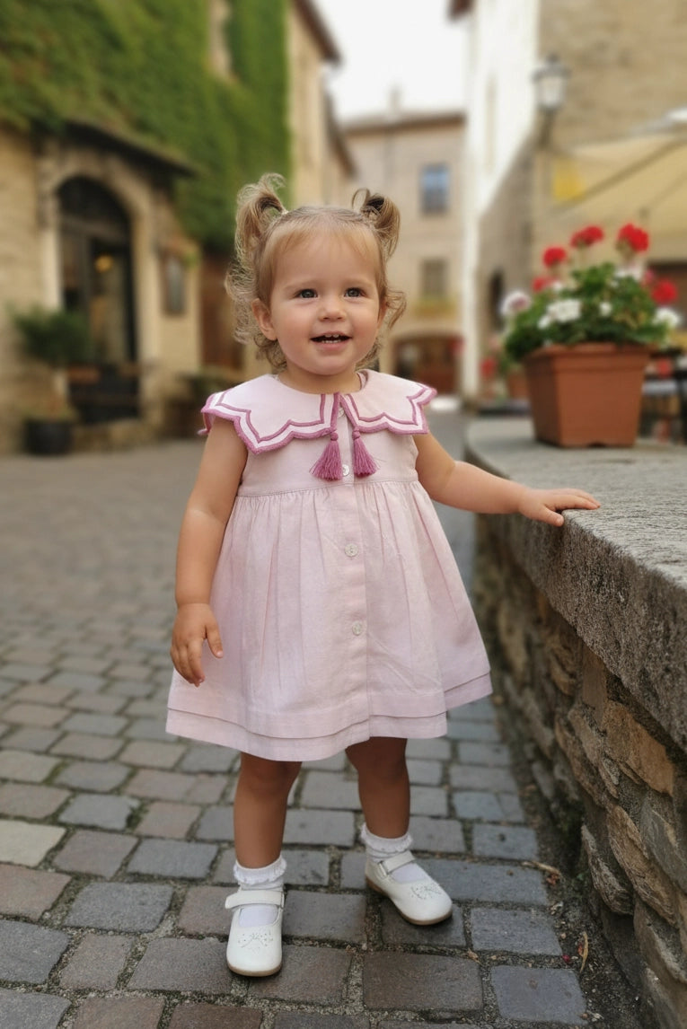 Young girl in a pink dress with a detailed collar and buttons. 