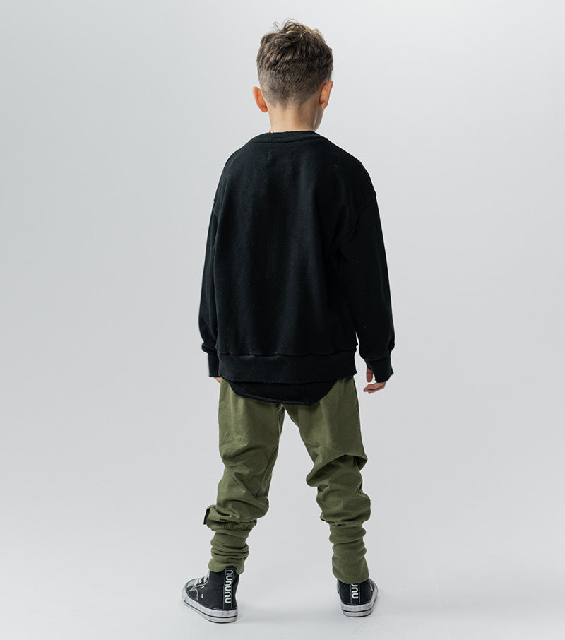 little boy standing backwards wearing a black shirt with green joggers