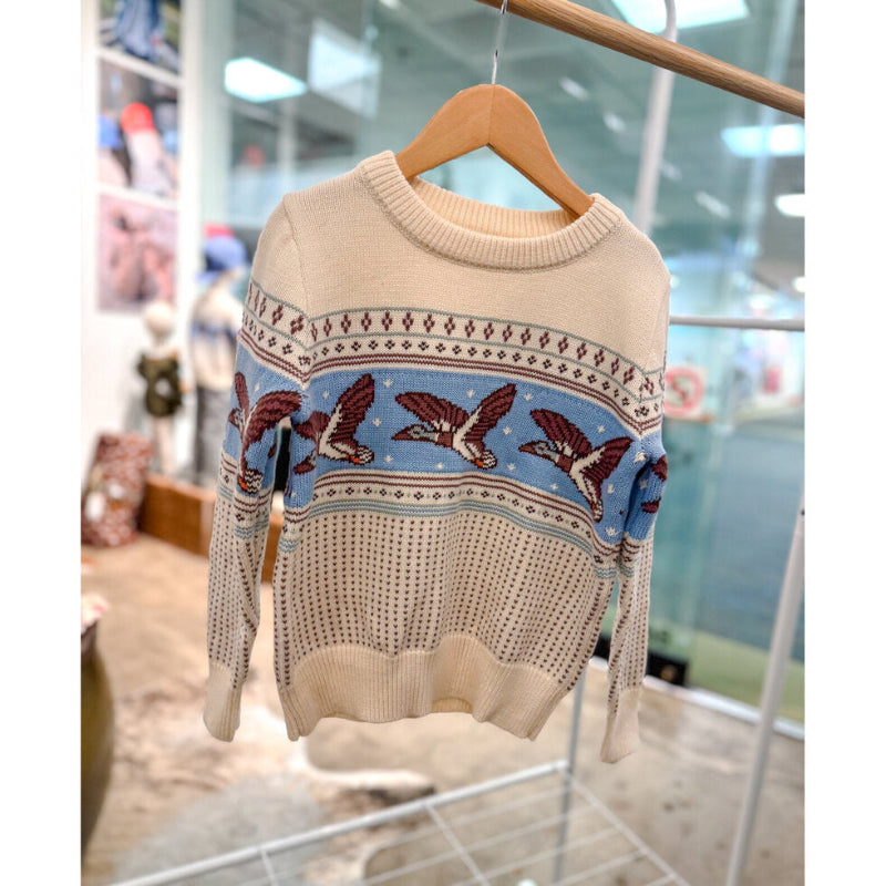 Beige sweater with bird pattern on a hanger in a store setting